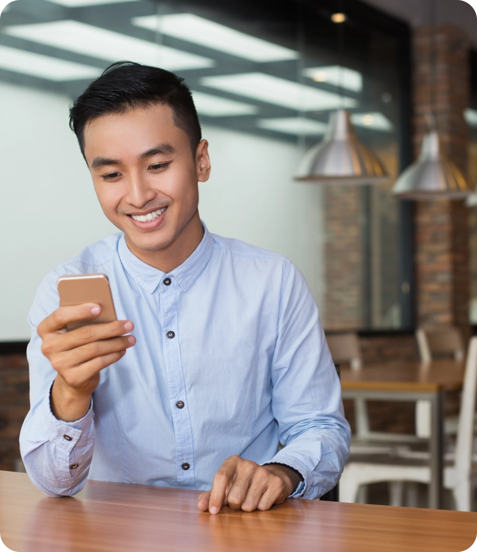smiling asian man using smartphone cafe table